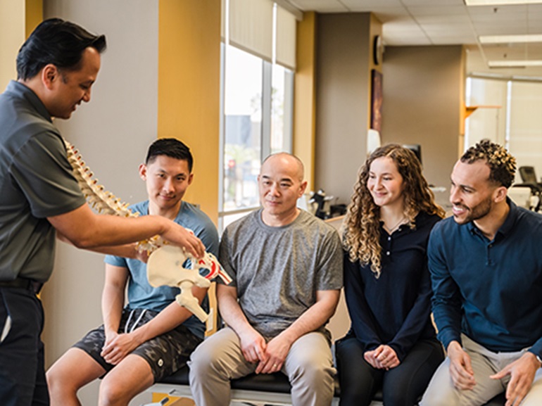 A physical therapist teaching students about the pelvic structure using a skeletal model.