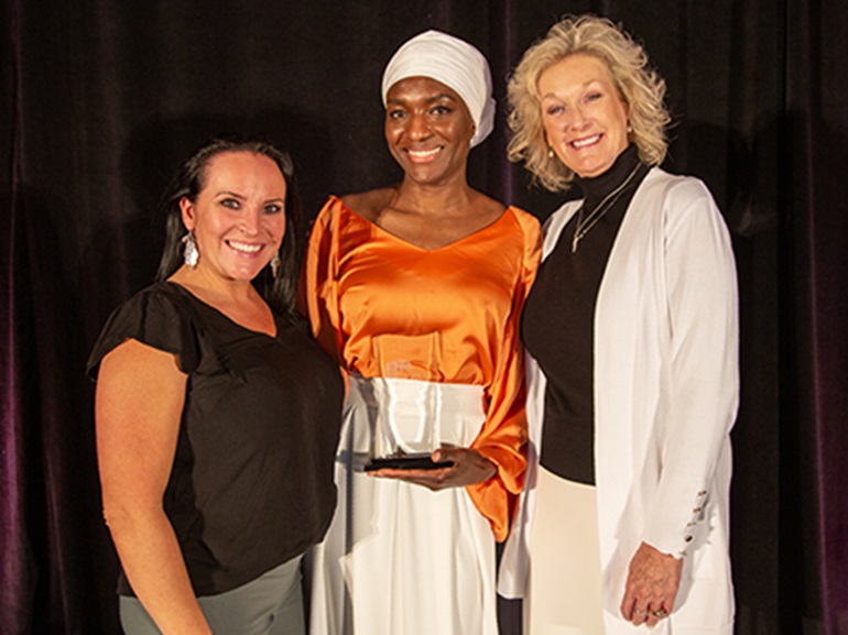A female award winner smiles and poses with her award with leadership.