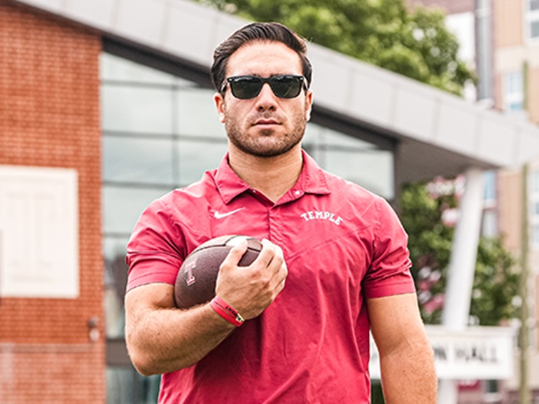 Residency leader stands holding a football, wearing a temple red shirt and sunglasses.