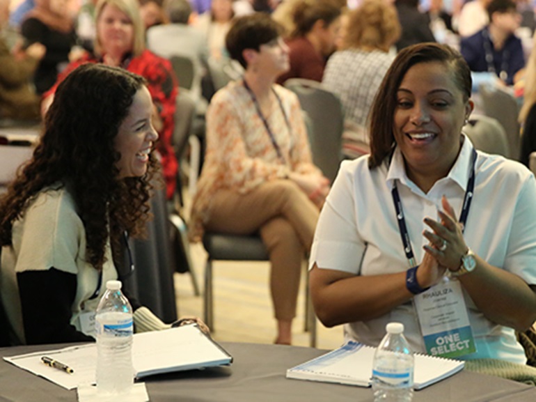 Two Select Medical employees laughing with each other at company conference.