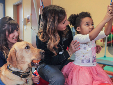 A female physical therapist working with a young, female pediatric patient and her therapy dog. 