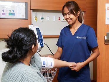 A nurse takes a patient's blood pressure while they sit on the edge of their hospital bed.