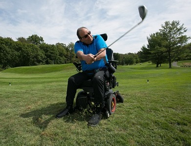 Jerry swings his golf club on a course while sitting in his wheelchair.