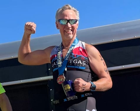 Bob, a Dignity Health Physical Therapy patient, flexes his bicep after winning his running race.